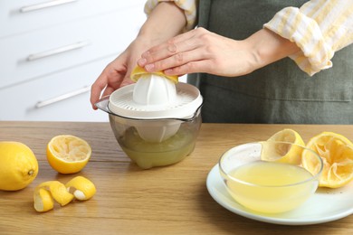 Photo of Woman with lemon using juicer at wooden table, closeup