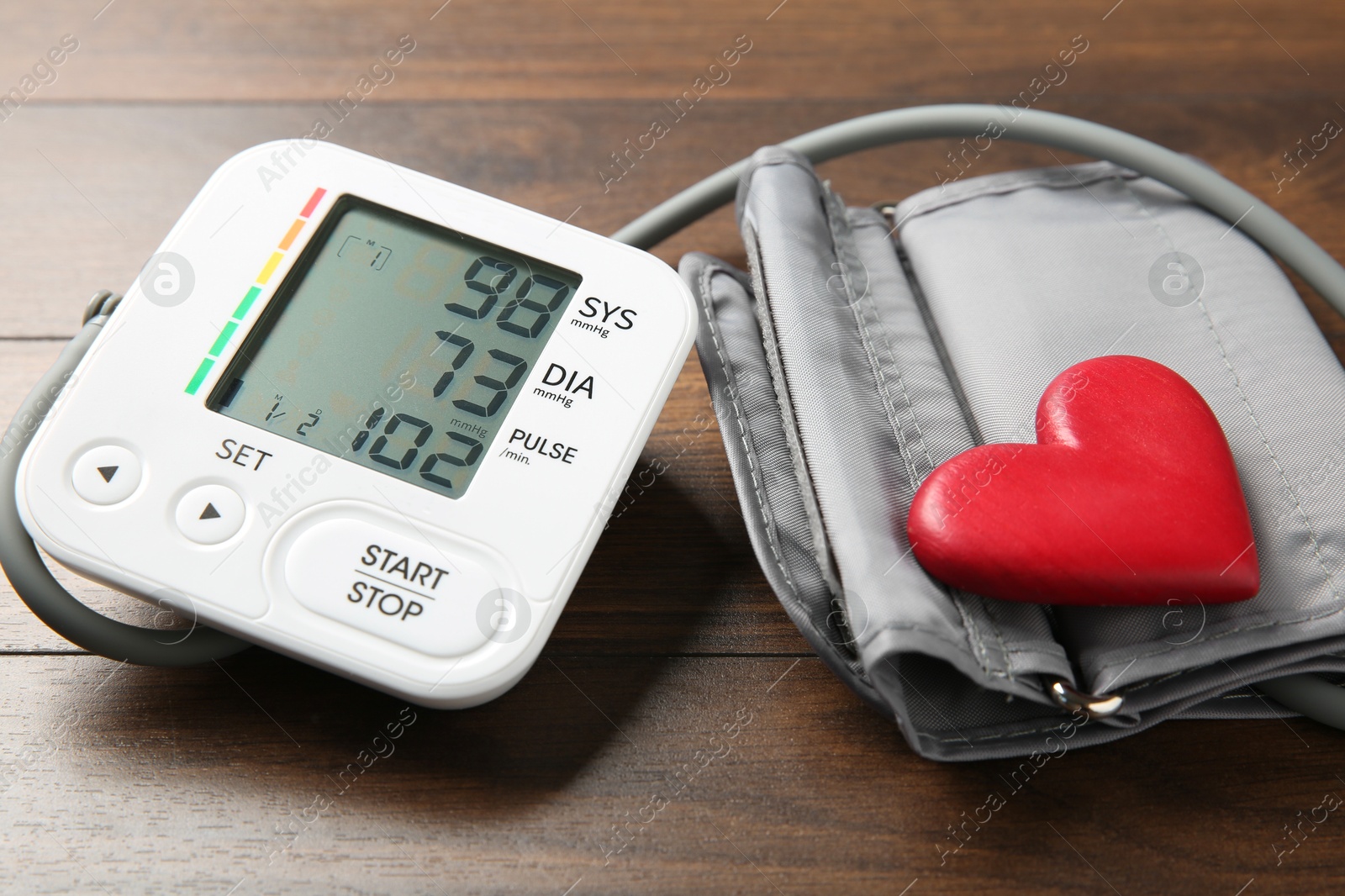 Photo of Blood pressure measuring device and heart figure on wooden table, closeup