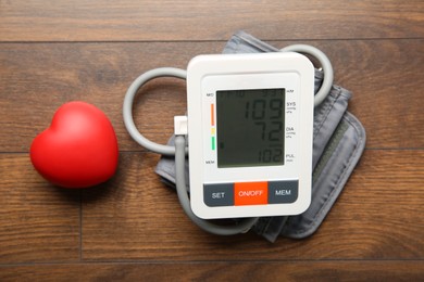 Photo of Blood pressure measuring device and squeeze heart on wooden table, top view