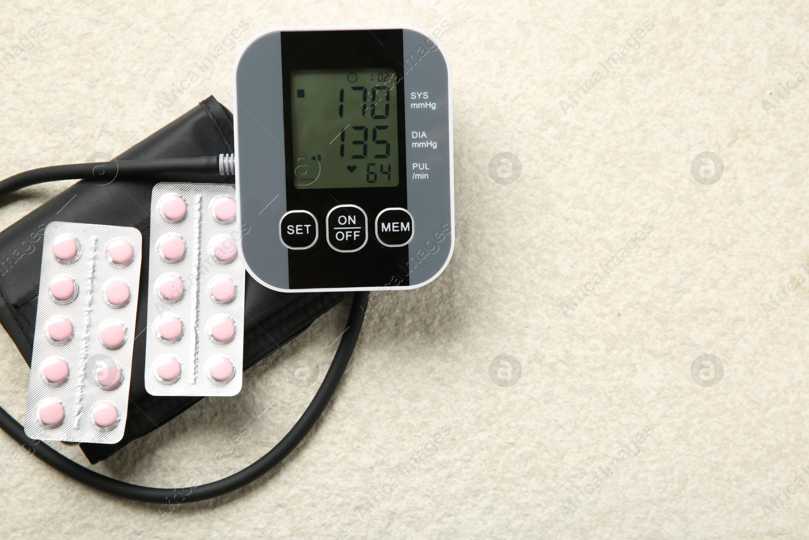 Photo of Blood pressure measuring device and pills on light textured background, top view. Space for text