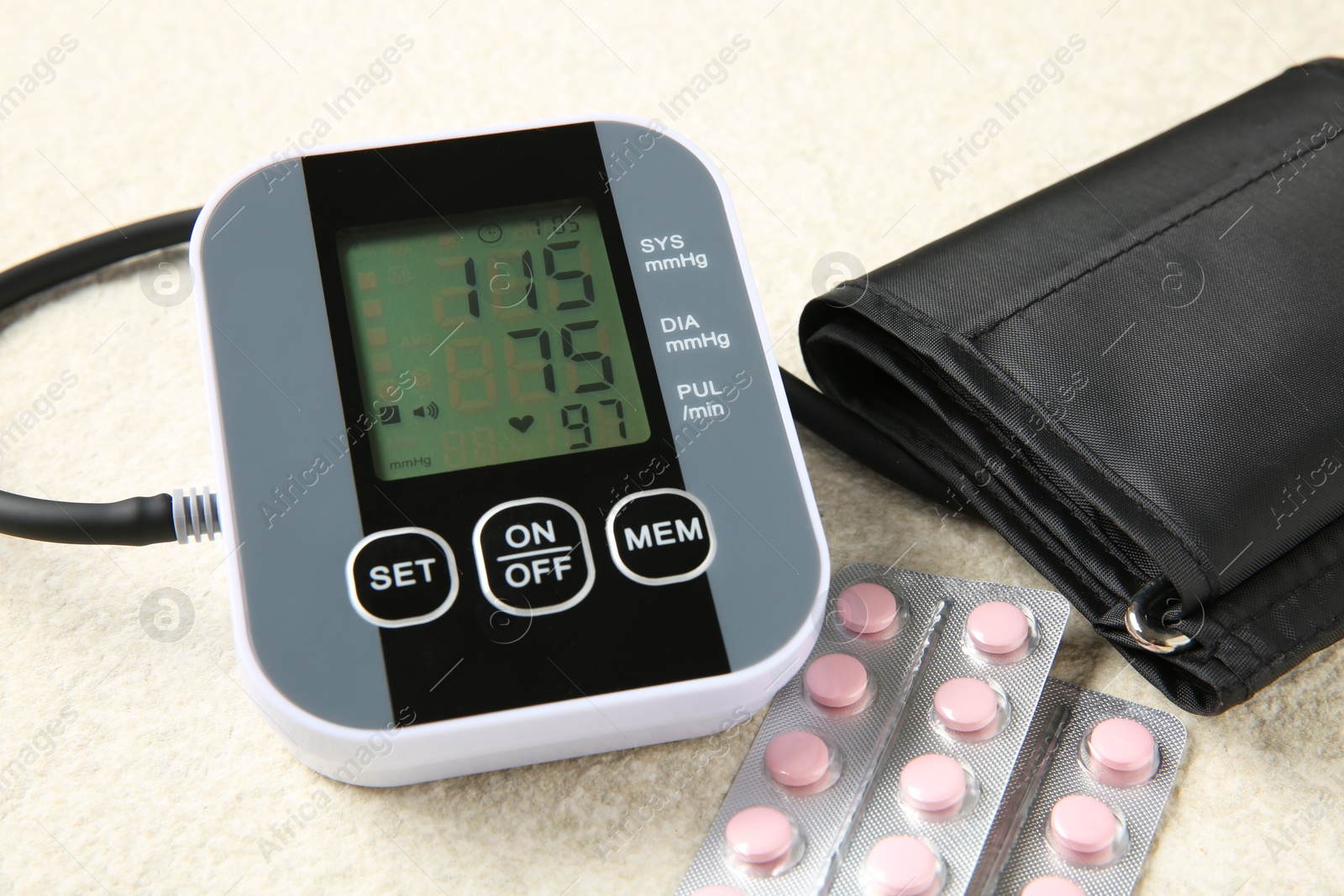 Photo of Blood pressure measuring device and pills on light textured background, closeup