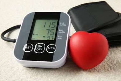 Photo of Blood pressure measuring device and squeeze heart on light textured background, closeup