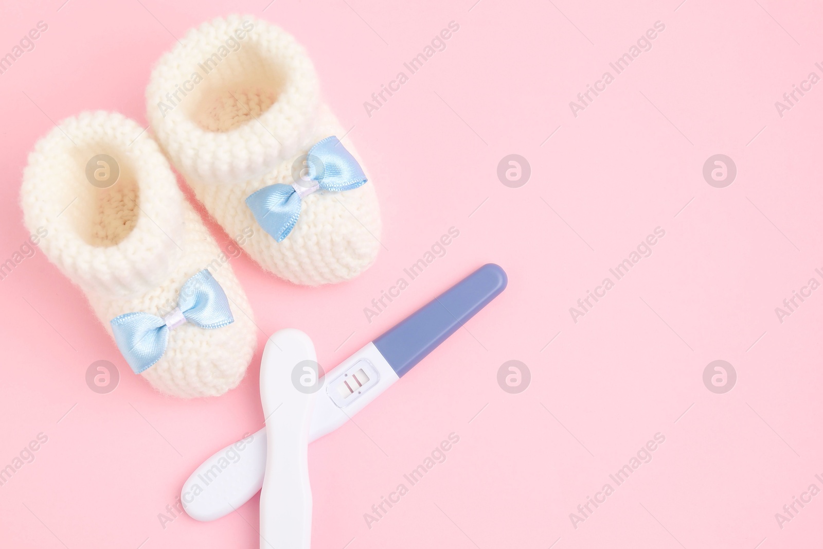 Photo of Pregnancy tests and knitted booties on pink background, top view. Space for text