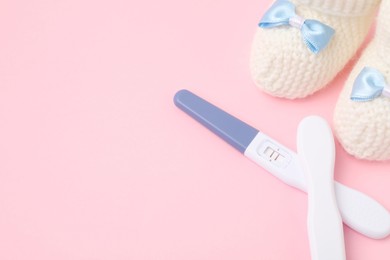 Photo of Pregnancy tests and knitted booties on pink background, closeup. Space for text