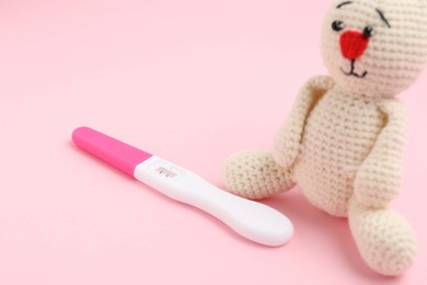 Photo of Pregnancy test and toy bunny on pink background, closeup