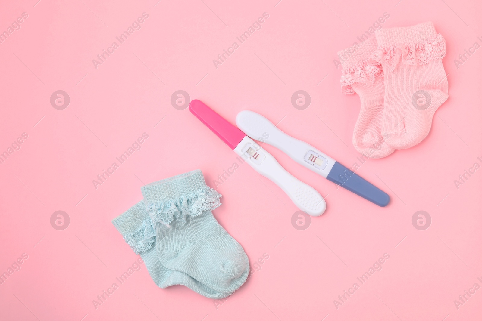 Photo of Pregnancy tests and socks on pink background, top view