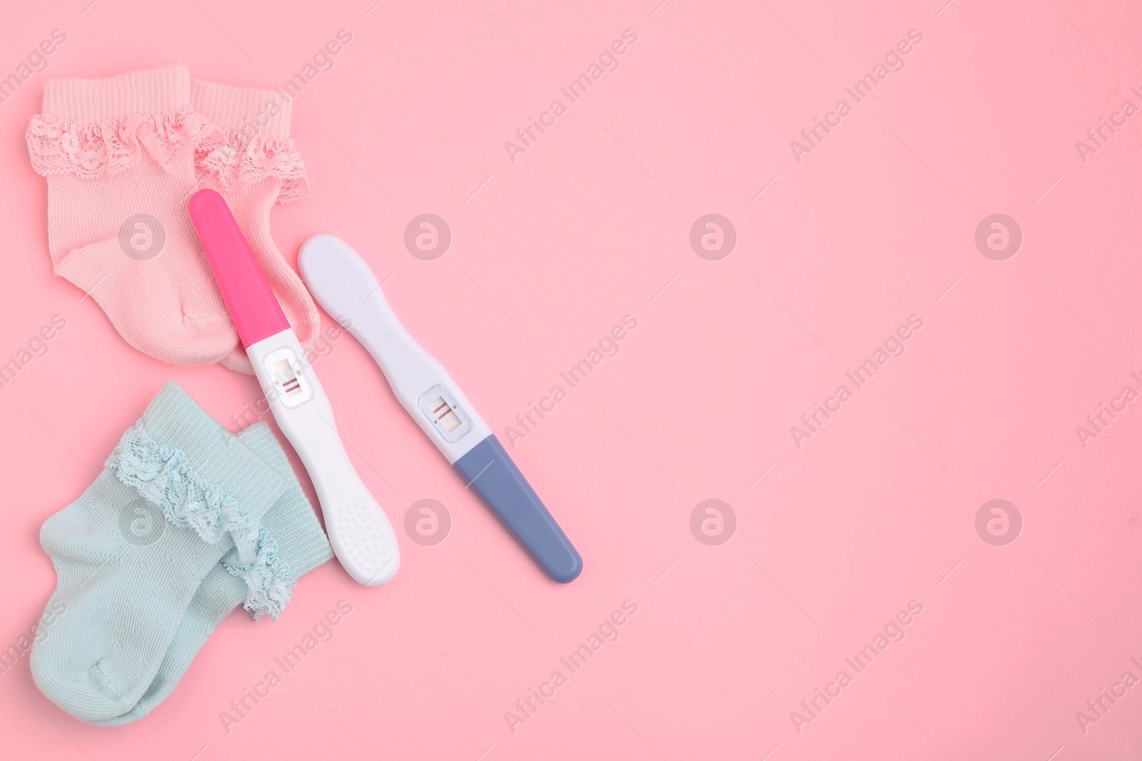 Photo of Pregnancy tests and socks on pink background, top view. Space for text