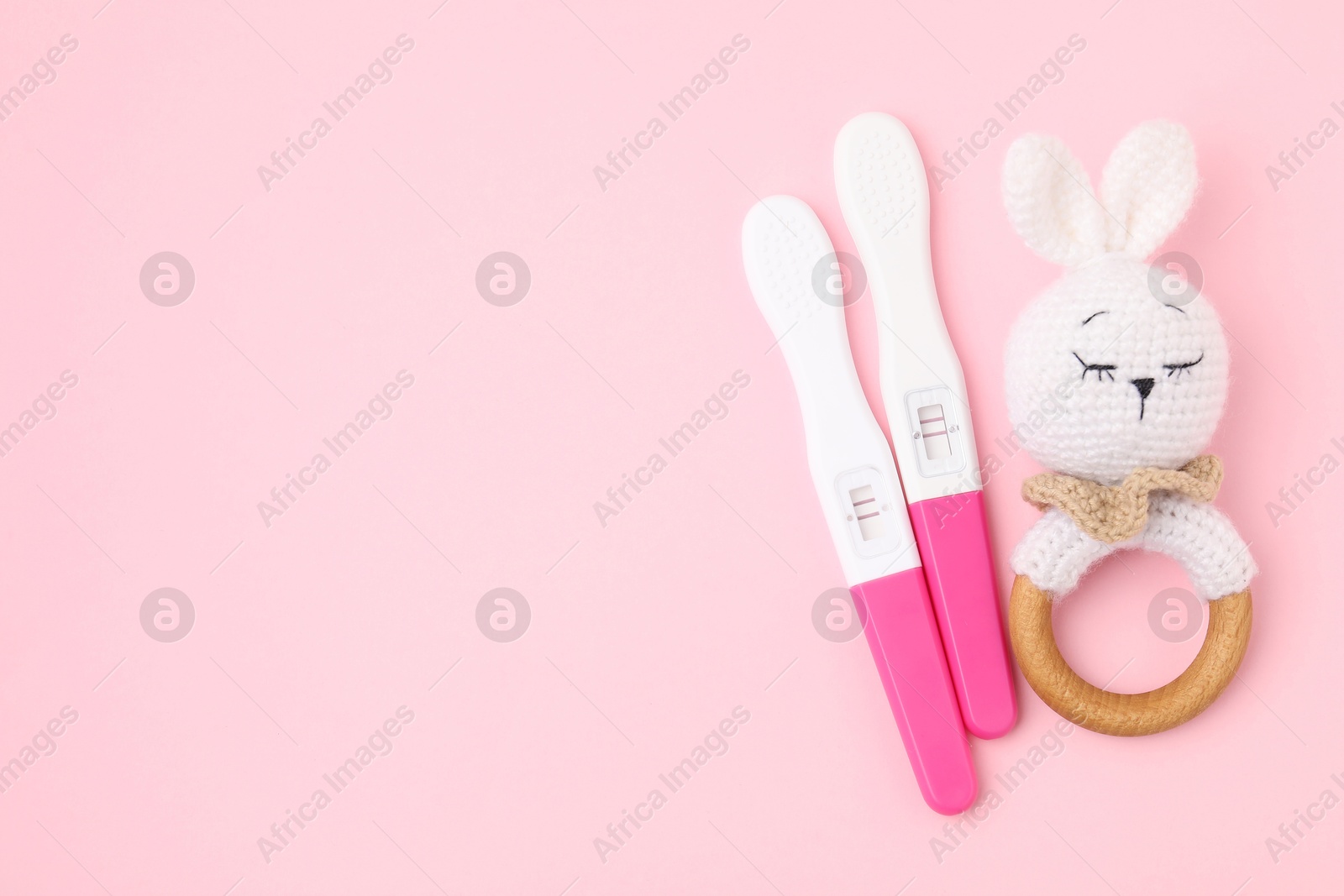 Photo of Pregnancy tests and baby rattle on pink background, top view. Space for text