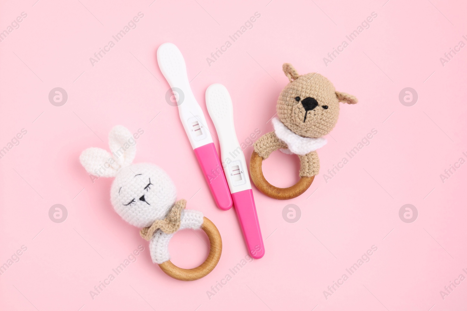 Photo of Pregnancy tests and baby rattles on pink background, top view