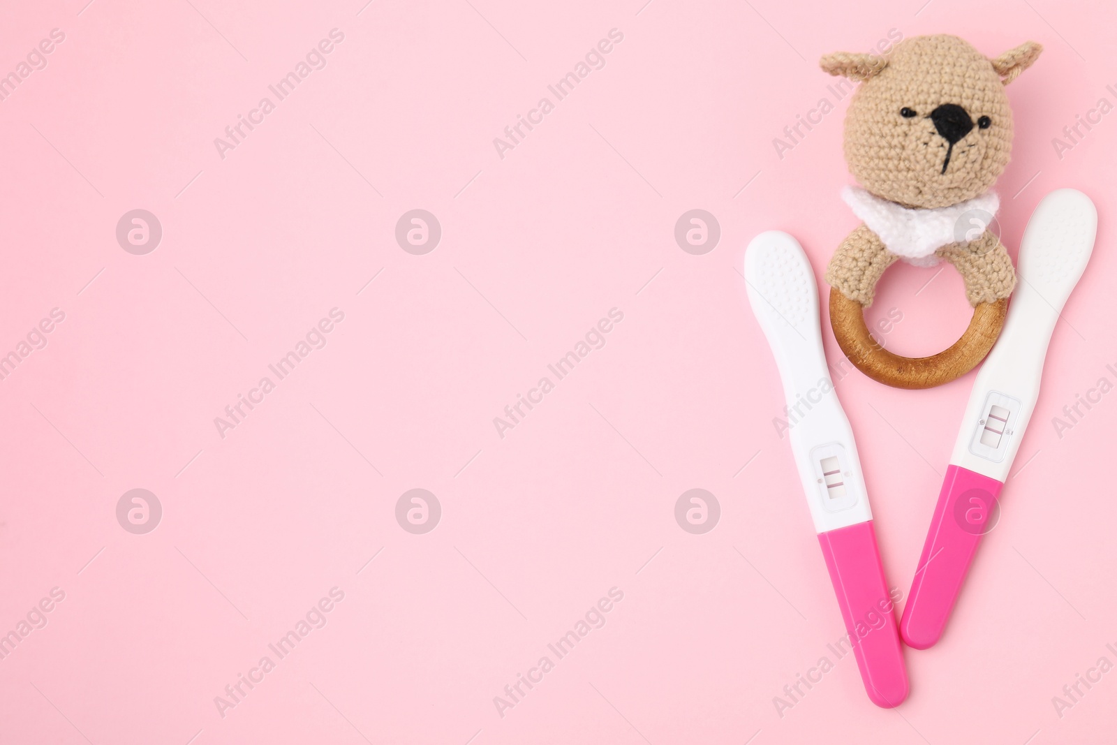 Photo of Pregnancy tests and baby rattle on pink background, top view. Space for text