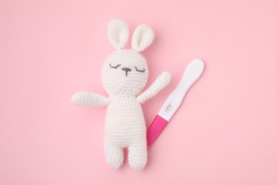 Photo of Pregnancy test and toy bunny on pink background, top view