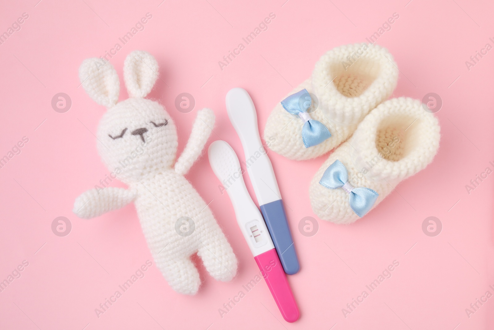 Photo of Pregnancy tests, toy bunny and knitted booties on pink background, top view