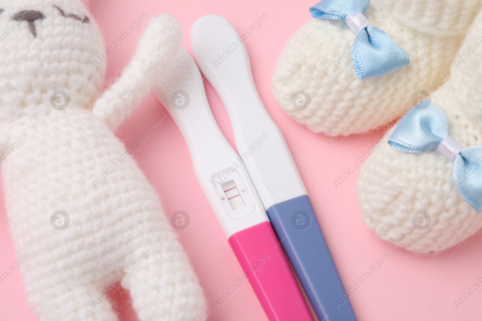 Photo of Pregnancy tests, toy bunny and knitted booties on pink background, closeup