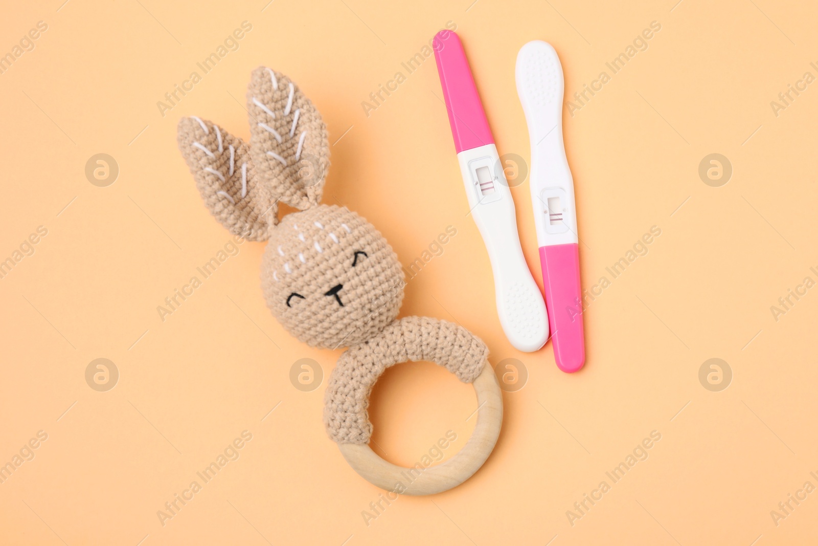 Photo of Pregnancy tests and baby rattle on pale orange background, top view