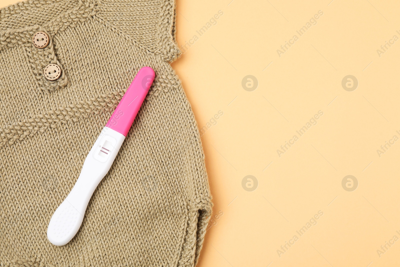 Photo of Pregnancy test and baby clothes on pale orange background, above view. Space for text