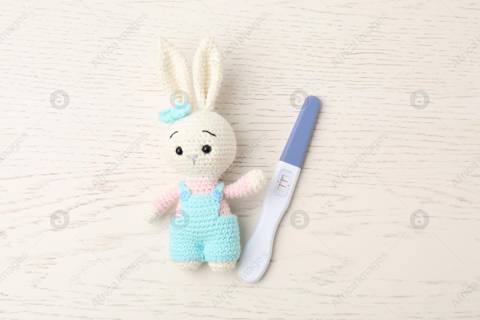 Photo of Pregnancy test and bunny toy on white wooden table, top view