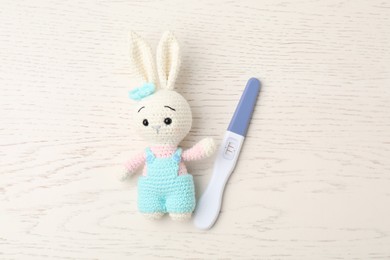 Photo of Pregnancy test and bunny toy on white wooden table, top view