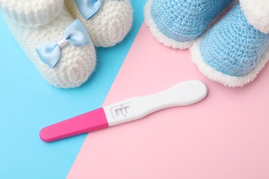 Photo of Pregnancy test and baby shoes on color background, above view