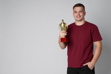 Photo of Happy winner with golden trophy cup on light grey background, space for text