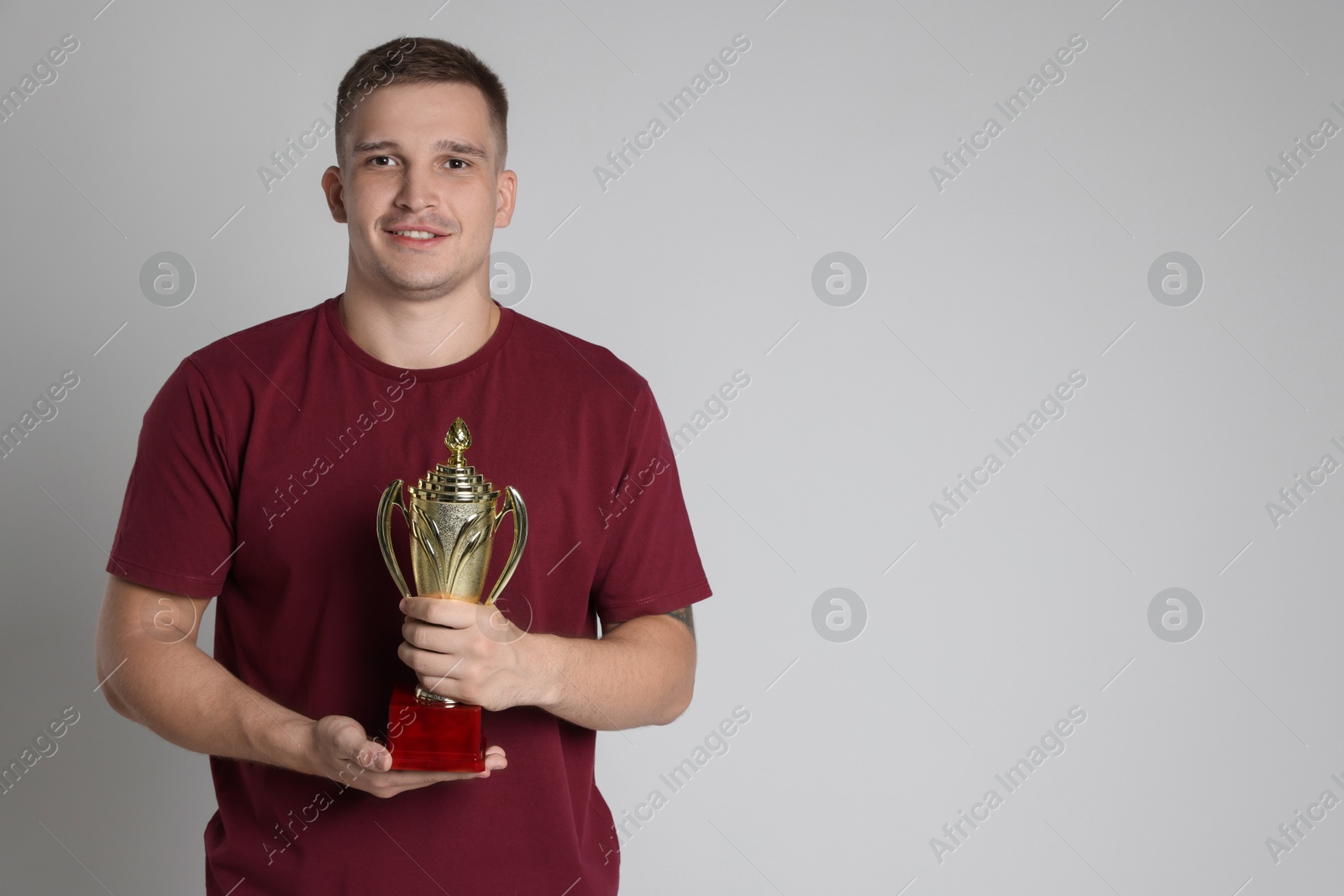 Photo of Happy winner with golden trophy cup on light grey background, space for text