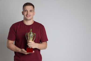 Happy winner with golden trophy cup on light grey background, space for text