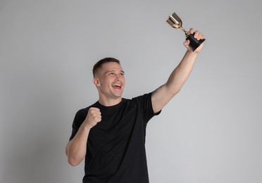 Photo of Happy winner with golden trophy cup on light grey background