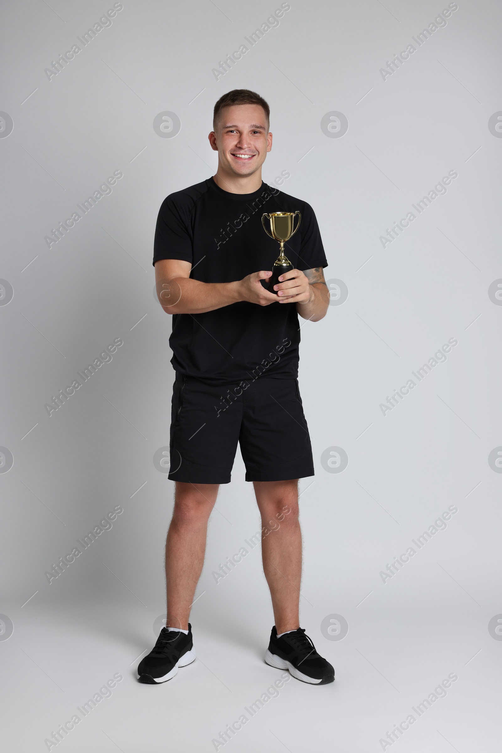 Photo of Happy winner with golden trophy cup on light grey background