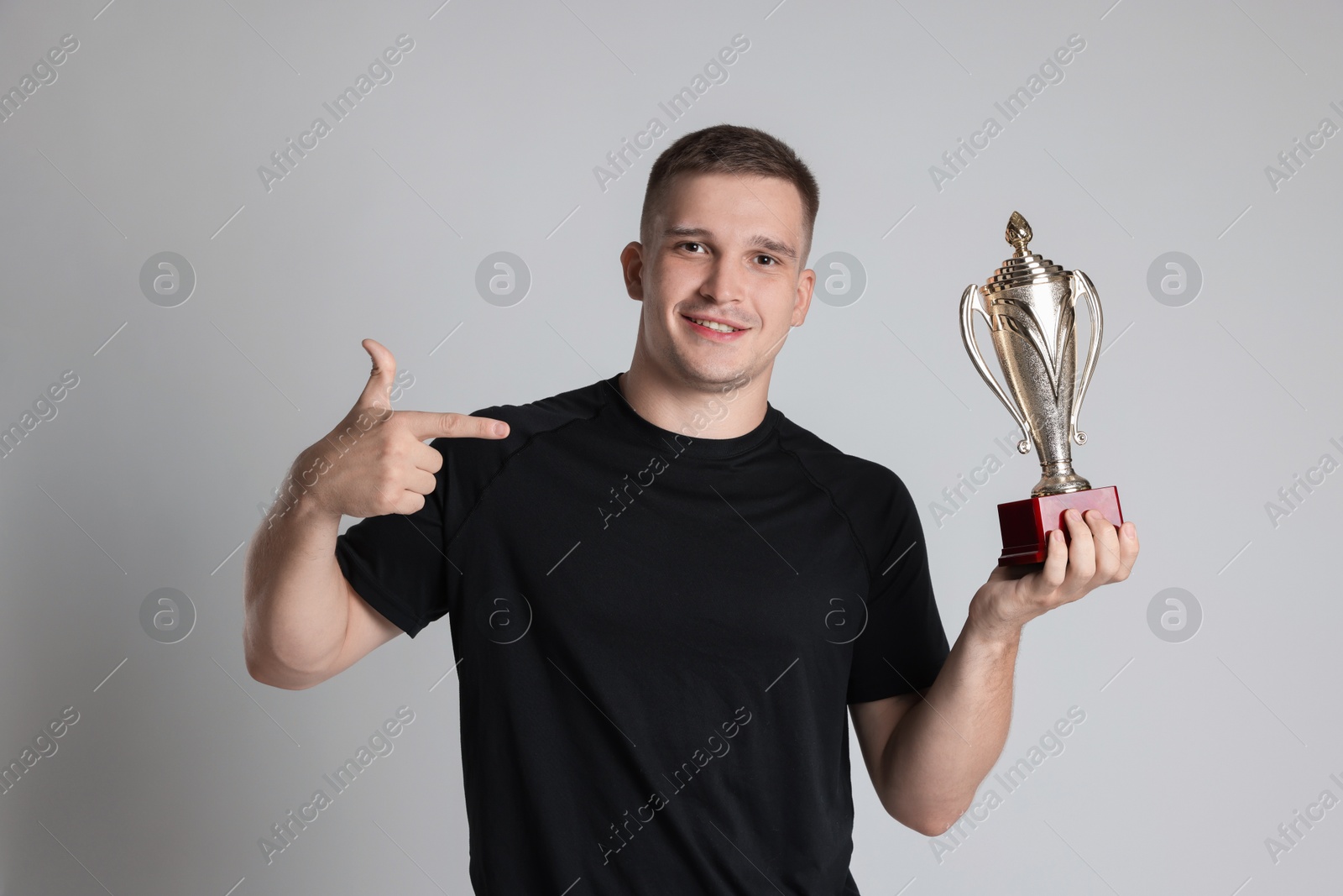 Photo of Happy winner with golden trophy cup on light grey background