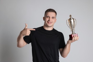 Photo of Happy winner with golden trophy cup on light grey background