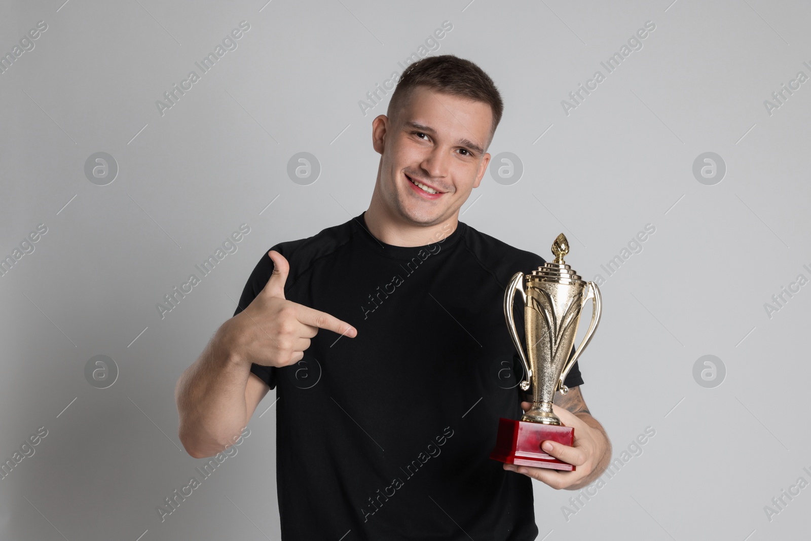 Photo of Happy winner with golden trophy cup on light grey background