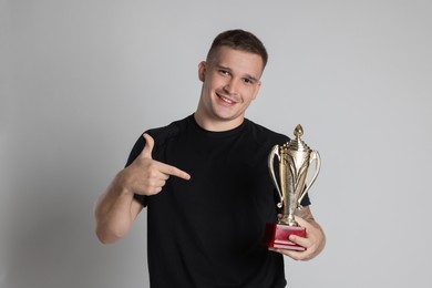 Photo of Happy winner with golden trophy cup on light grey background