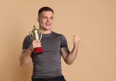 Photo of Happy winner with golden trophy cup on beige background