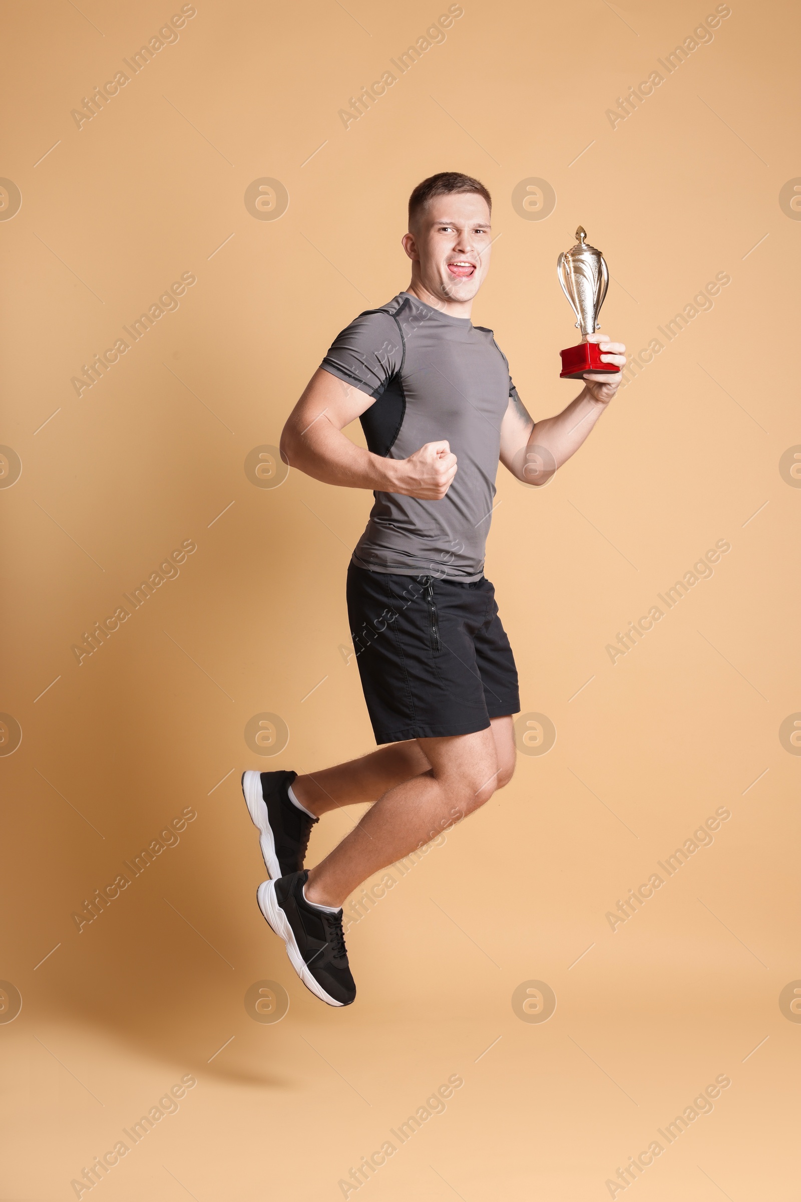 Photo of Happy winner with golden trophy cup jumping on beige background