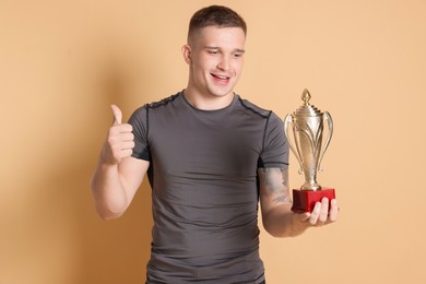 Photo of Happy winner with golden trophy cup showing thumbs up on beige background