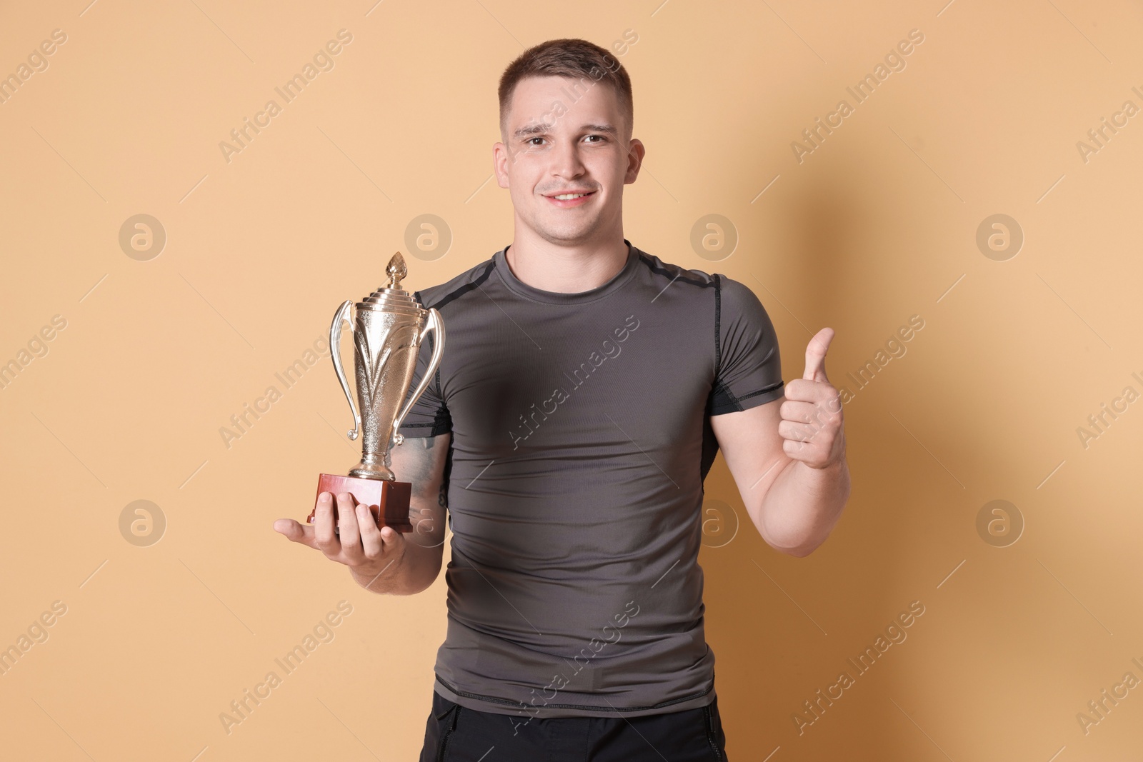 Photo of Happy winner with golden trophy cup showing thumbs up on beige background