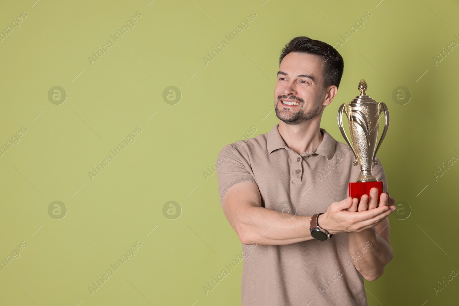 Photo of Happy winner with golden trophy cup on pale olive background, space for text