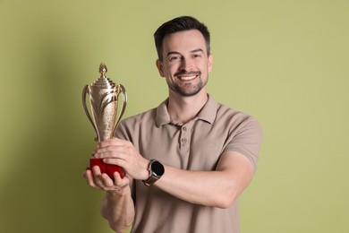 Photo of Happy winner with golden trophy cup on pale olive background