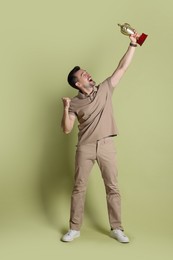 Photo of Happy winner with golden trophy cup on pale olive background