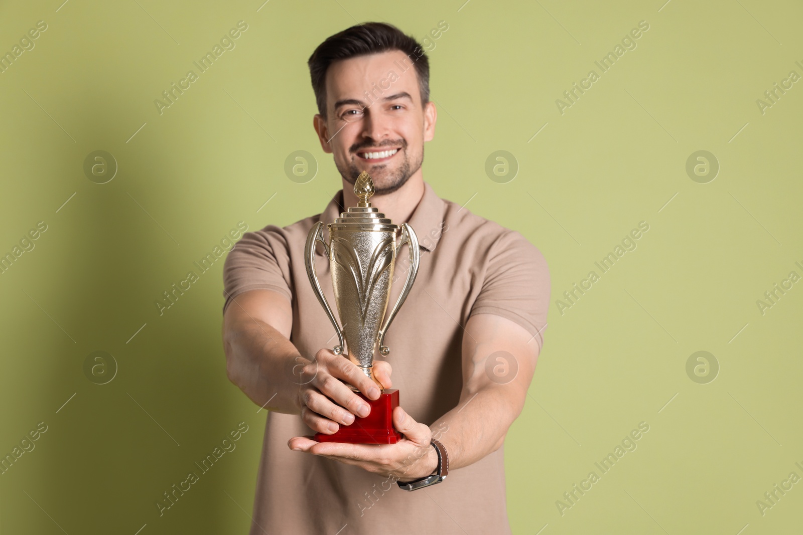 Photo of Happy winner with golden trophy cup on pale olive background