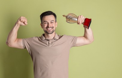 Photo of Happy winner with golden trophy cup showing his biceps on pale olive background