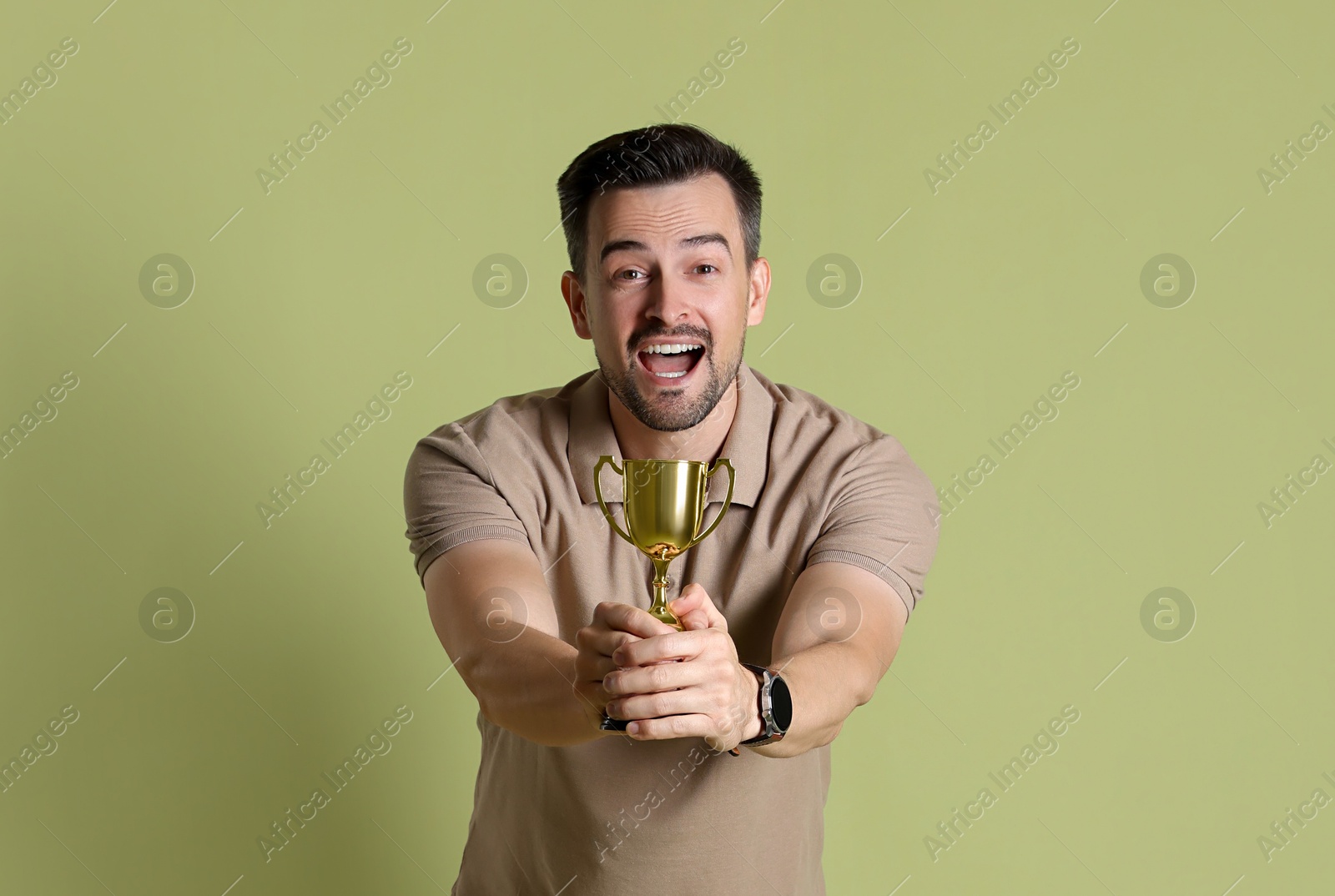 Photo of Happy winner with golden trophy cup on pale olive background