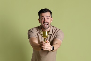 Happy winner with golden trophy cup on pale olive background