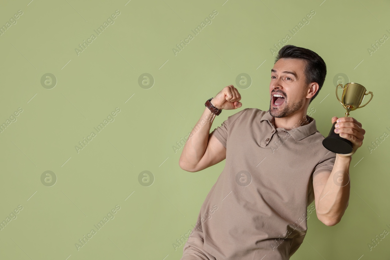 Photo of Happy winner with golden trophy cup on pale olive background, space for text