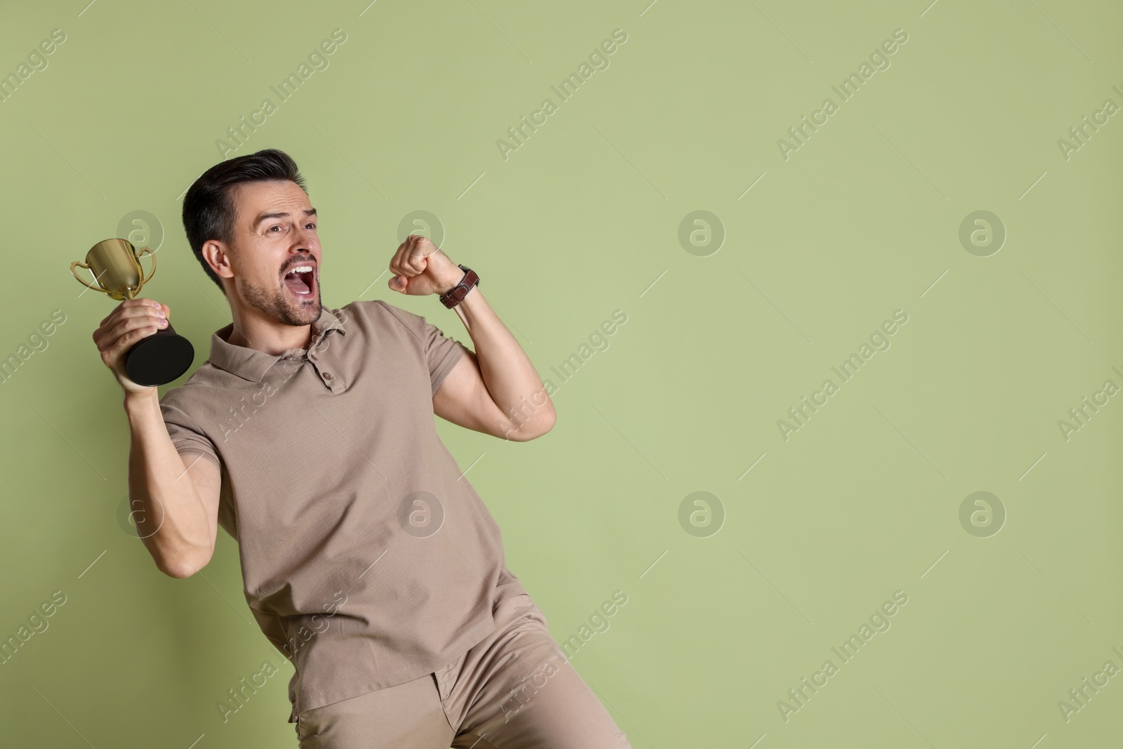 Photo of Happy winner with golden trophy cup on pale olive background, space for text