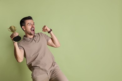 Photo of Happy winner with golden trophy cup on pale olive background, space for text