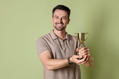 Photo of Happy winner with golden trophy cup on pale olive background