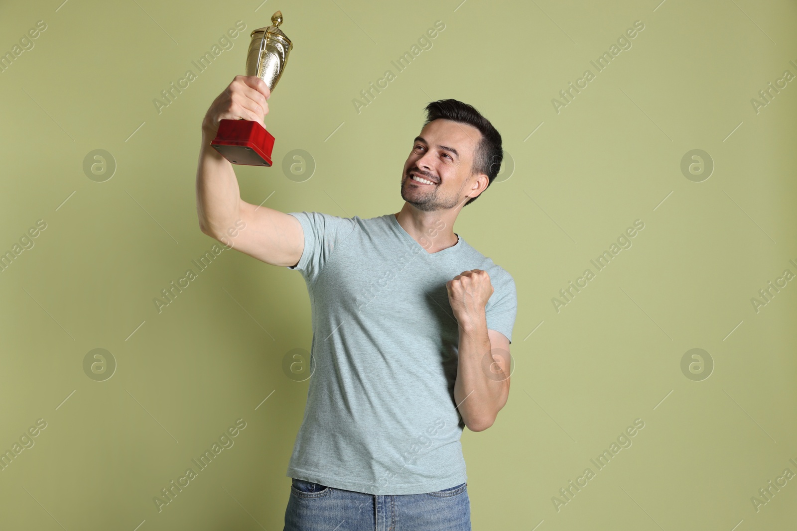 Photo of Happy winner with golden trophy cup on pale olive background