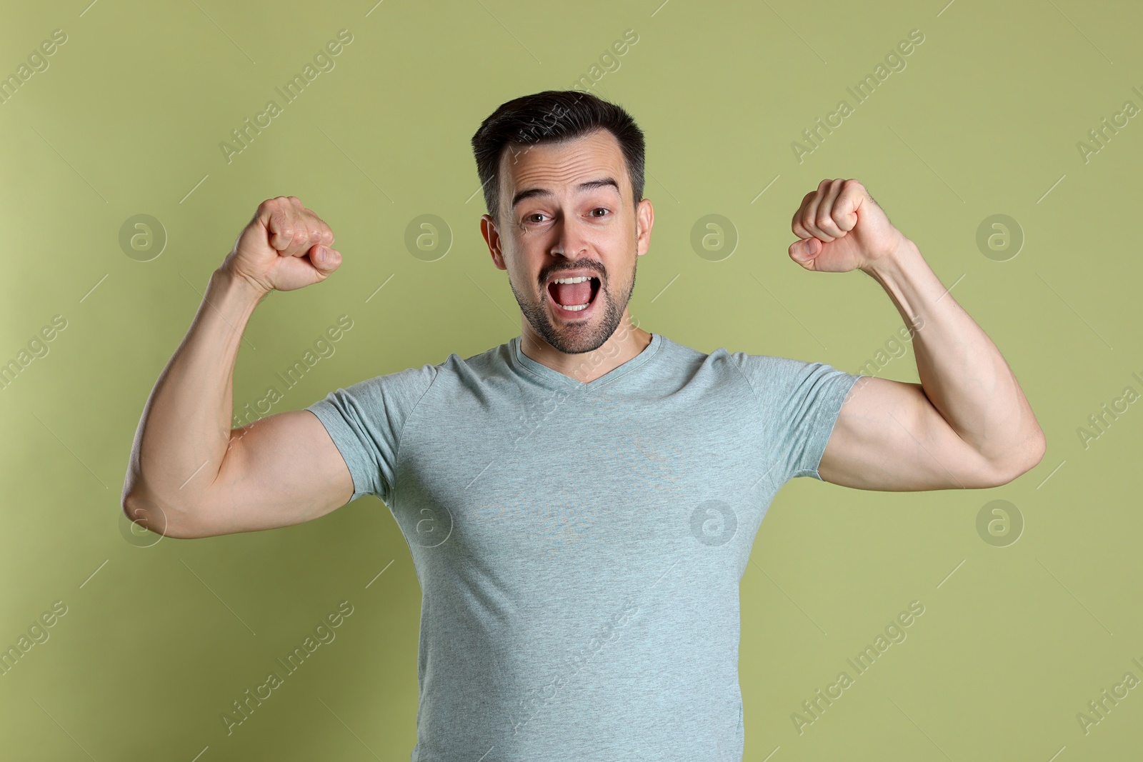 Photo of Happy winner showing his biceps on pale olive background