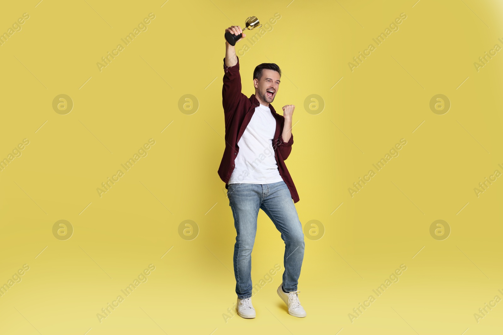 Photo of Happy winner with golden trophy cup on yellow background