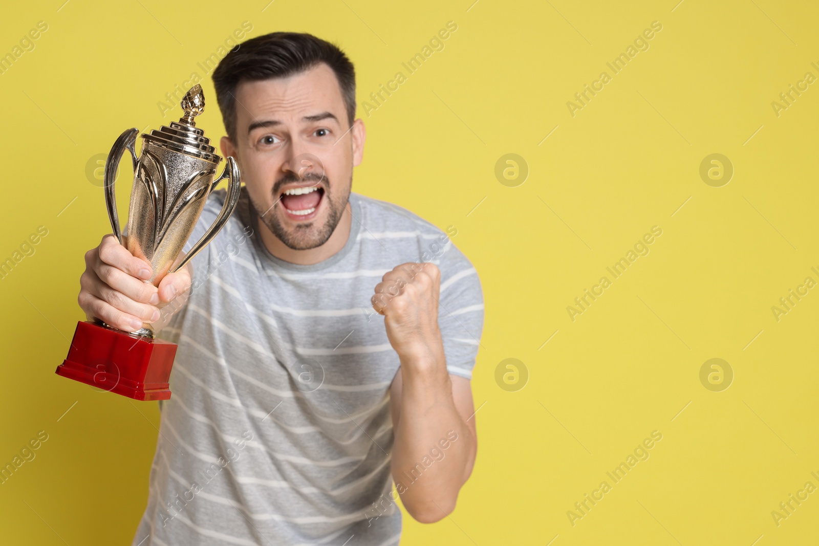 Photo of Happy winner with golden trophy cup on yellow background, space for text